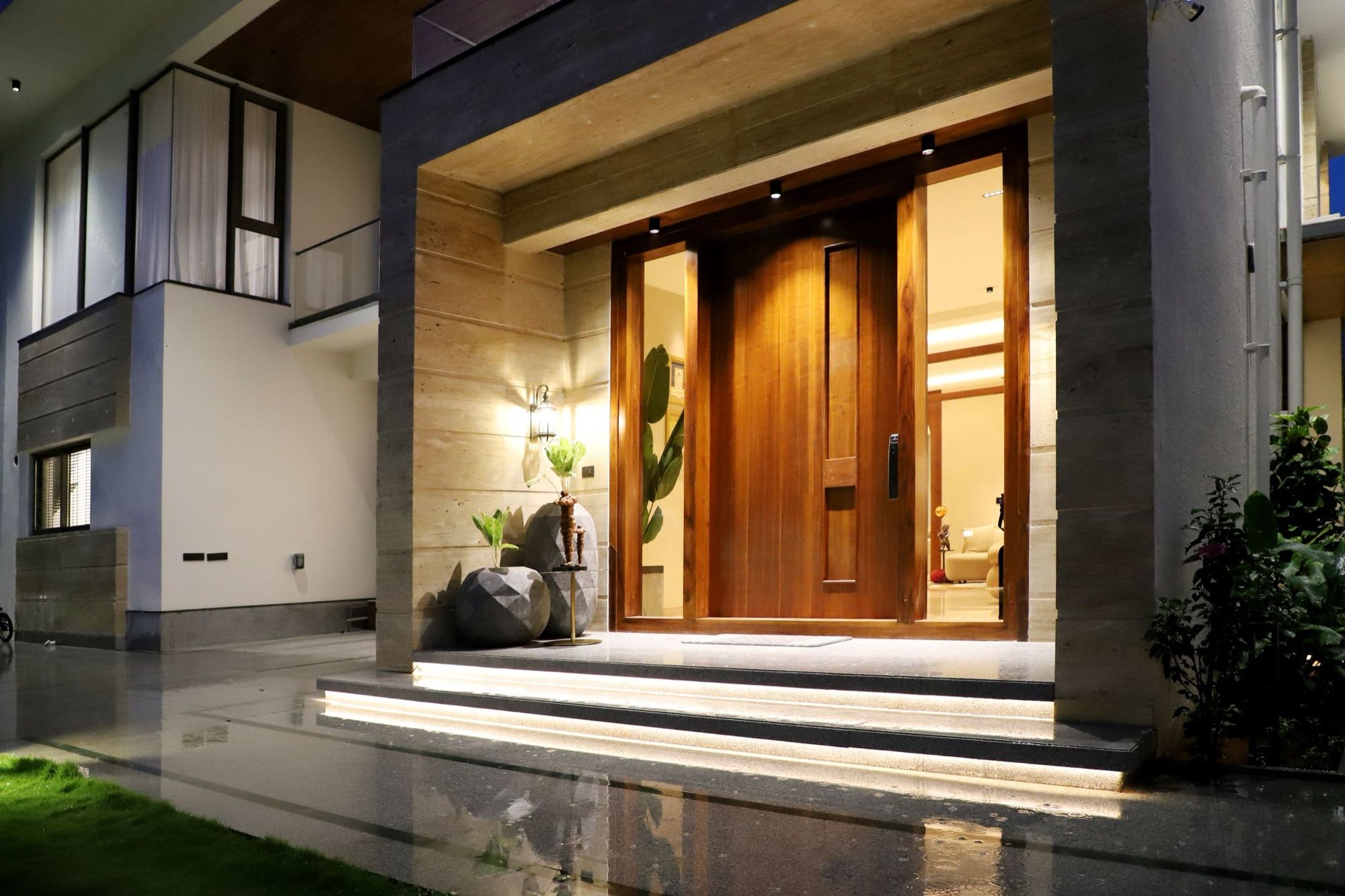 A modern entrance with a tall wooden door, warmly lit