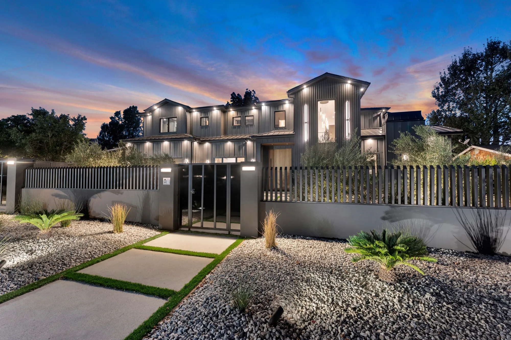 The house at dusk behind its slatted gate, every window lit